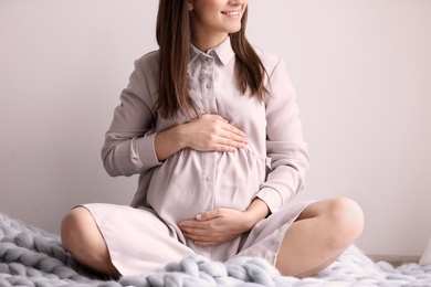 Young pregnant woman sitting on warm blanket indoors