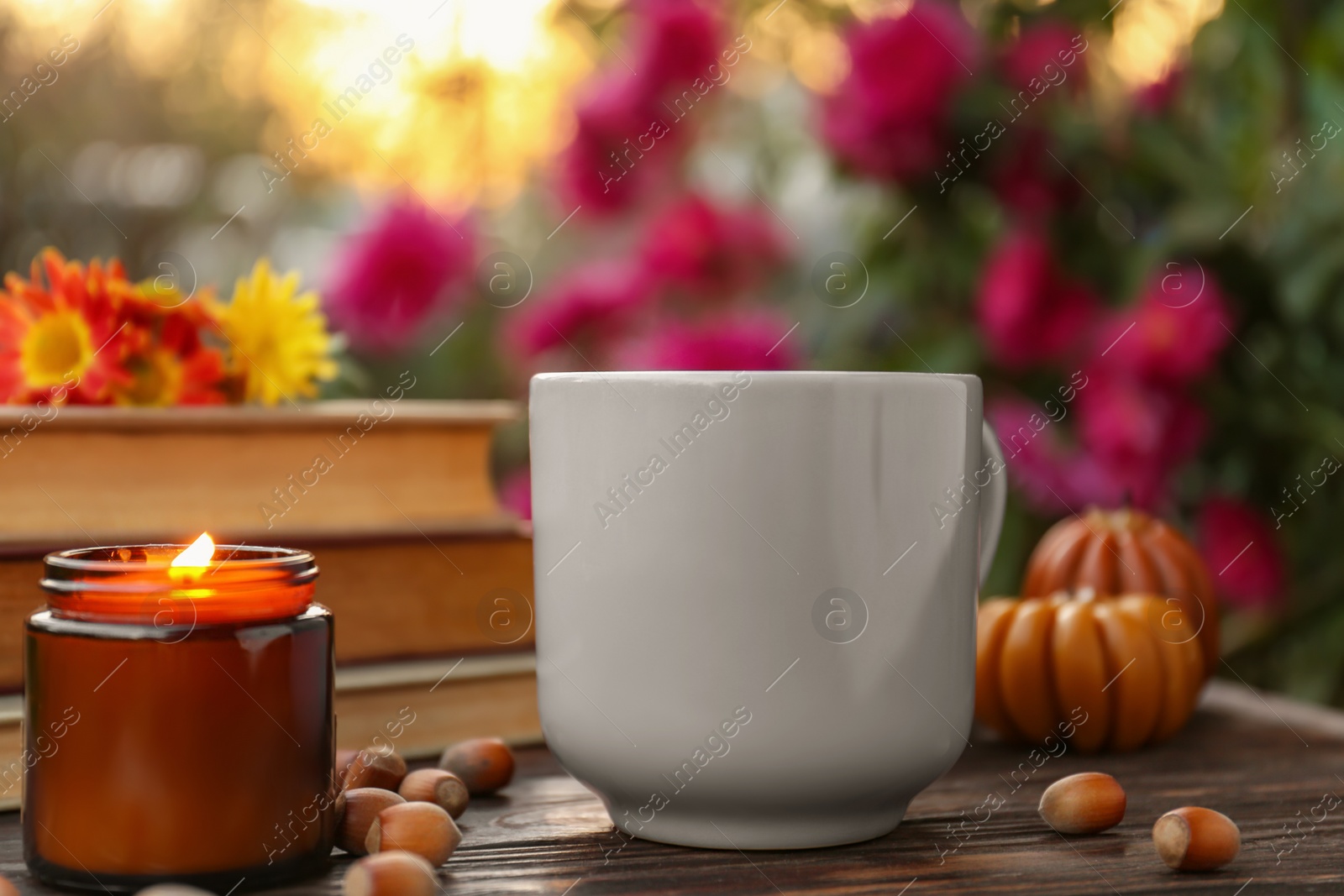 Photo of Cup of hot drink and burning candle on wooden table outdoors, closeup. Cozy autumn