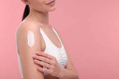 Photo of Woman with smear of body cream on her shoulder against pink background, closeup. Space for text