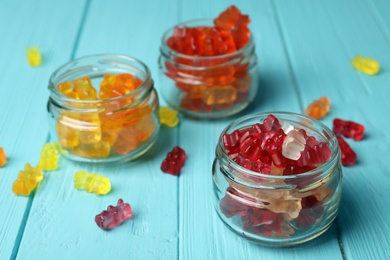 Photo of Three glass jars with delicious jelly bears on wooden table