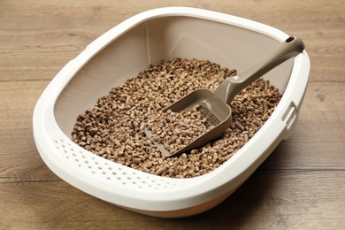 Cat litter tray with filler and scoop on wooden floor, closeup