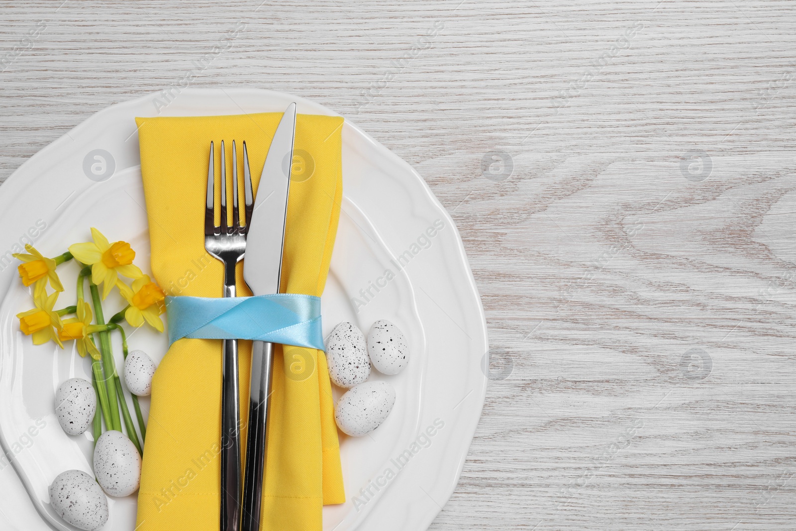 Photo of Festive table setting with painted eggs and cutlery on white wooden background, top view with space for text. Easter celebration