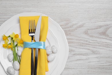 Festive table setting with painted eggs and cutlery on white wooden background, top view with space for text. Easter celebration