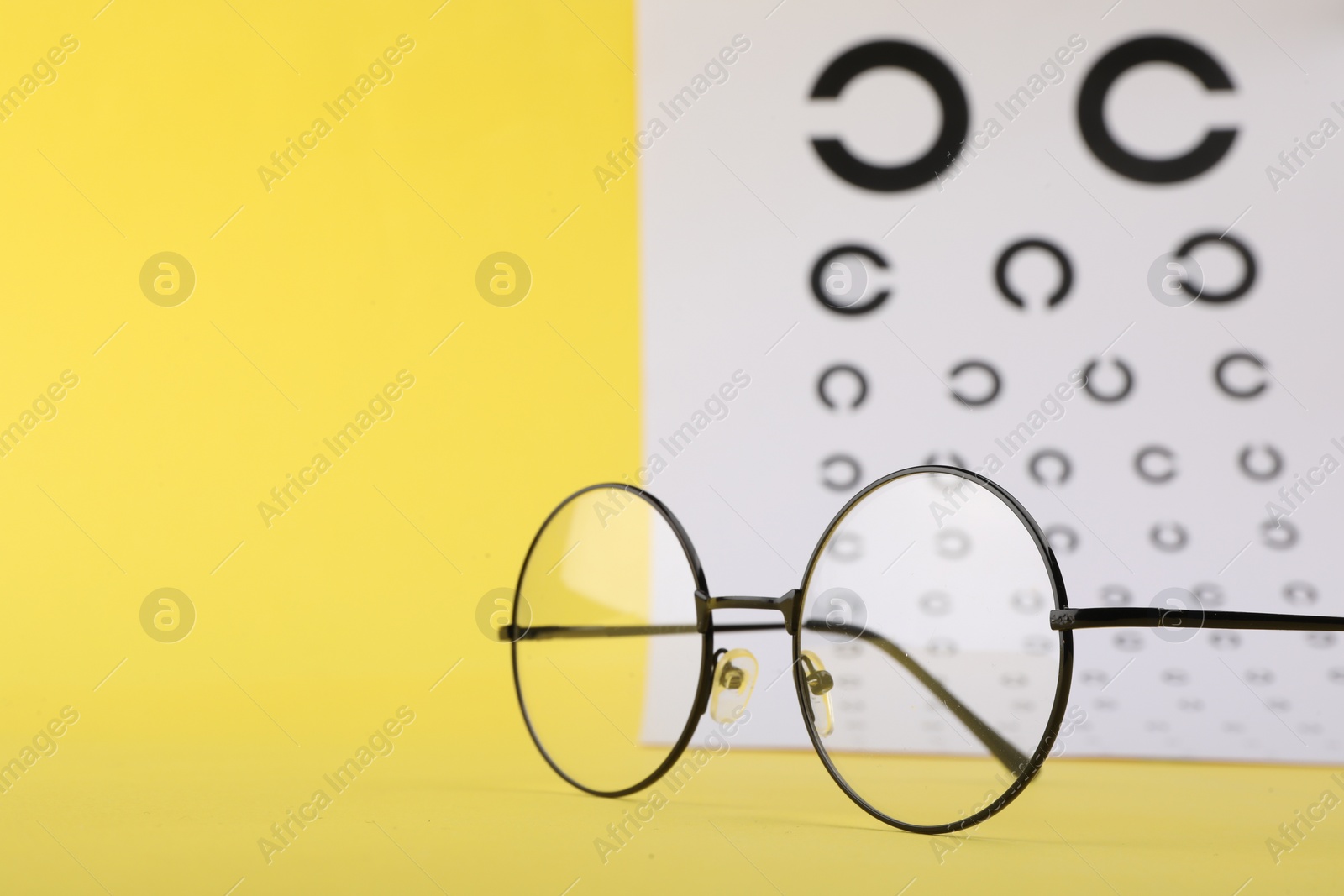 Photo of Vision test chart and glasses on yellow background, closeup. Space for text