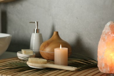 Photo of Composition with different spa products, burning candle and Himalayan salt lamp on countertop in bathroom