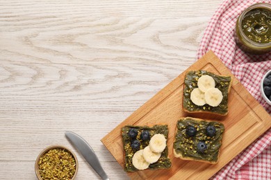 Photo of Toasts with tasty pistachio butter, banana slices, blueberries and nuts on white wooden table, flat lay. Space for text