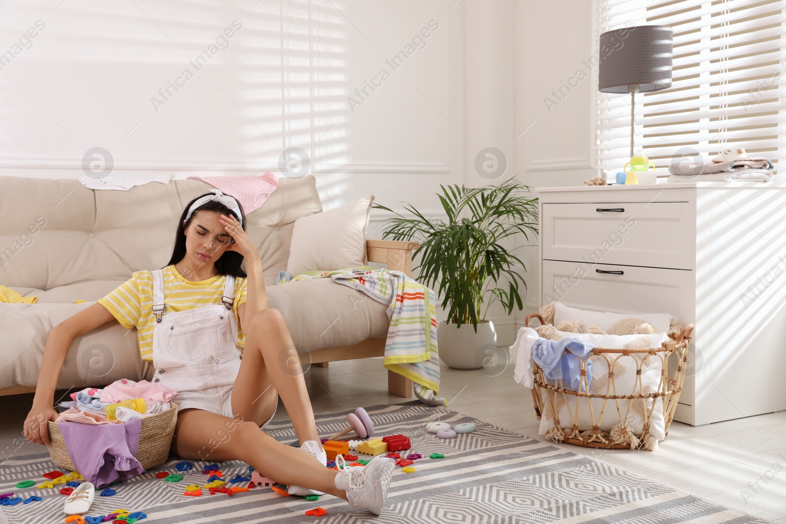 Photo of Tired young mother sitting on floor in messy living room