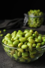 Photo of Bowl of delicious edamame beans on grey table against dark background, closeup