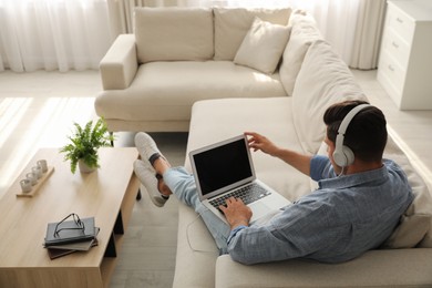 Man with laptop and headphones sitting on sofa at home