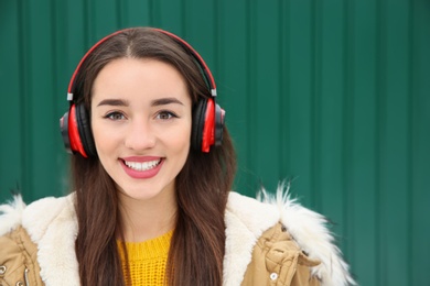 Beautiful young woman listening to music with headphones against color wall. Space for text