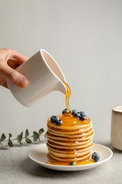 Woman pouring honey onto tasty pancakes with berries on table, closeup