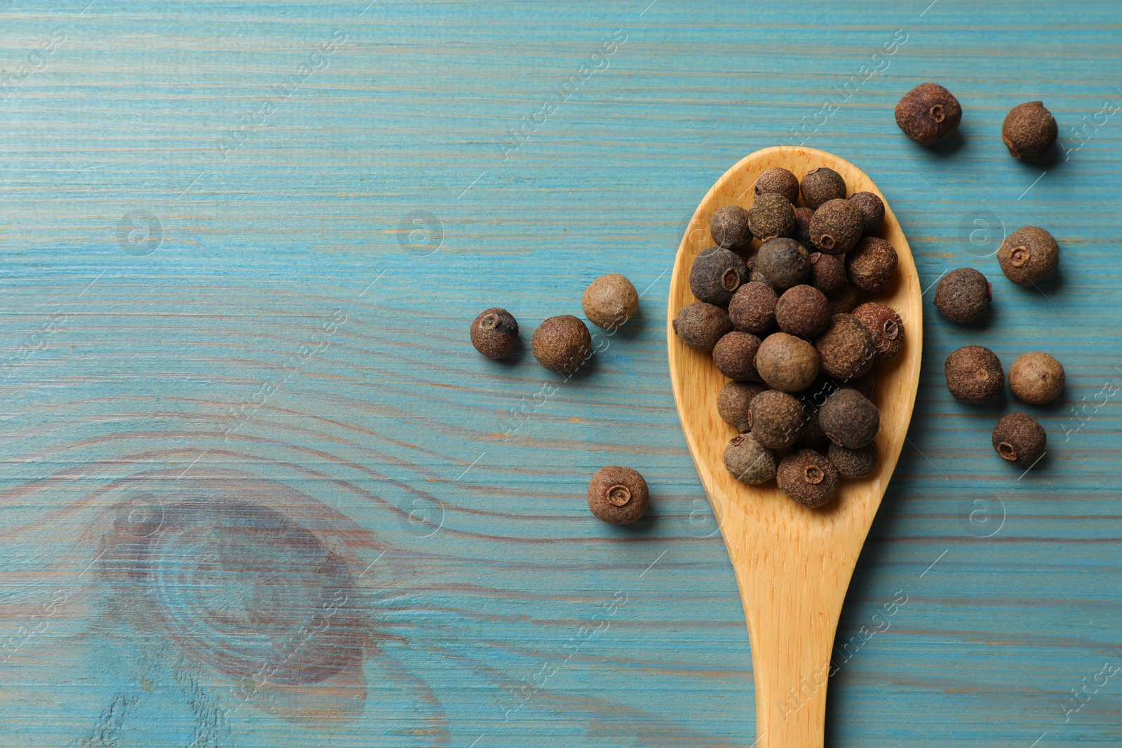 Photo of Aromatic allspice pepper grains and spoon on light blue wooden table, top view. Space for text