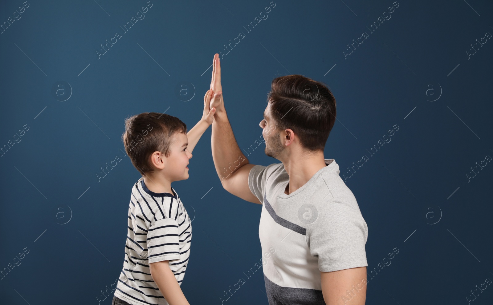 Photo of Portrait of dad and his son giving high five on color background