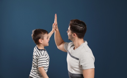 Photo of Portrait of dad and his son giving high five on color background