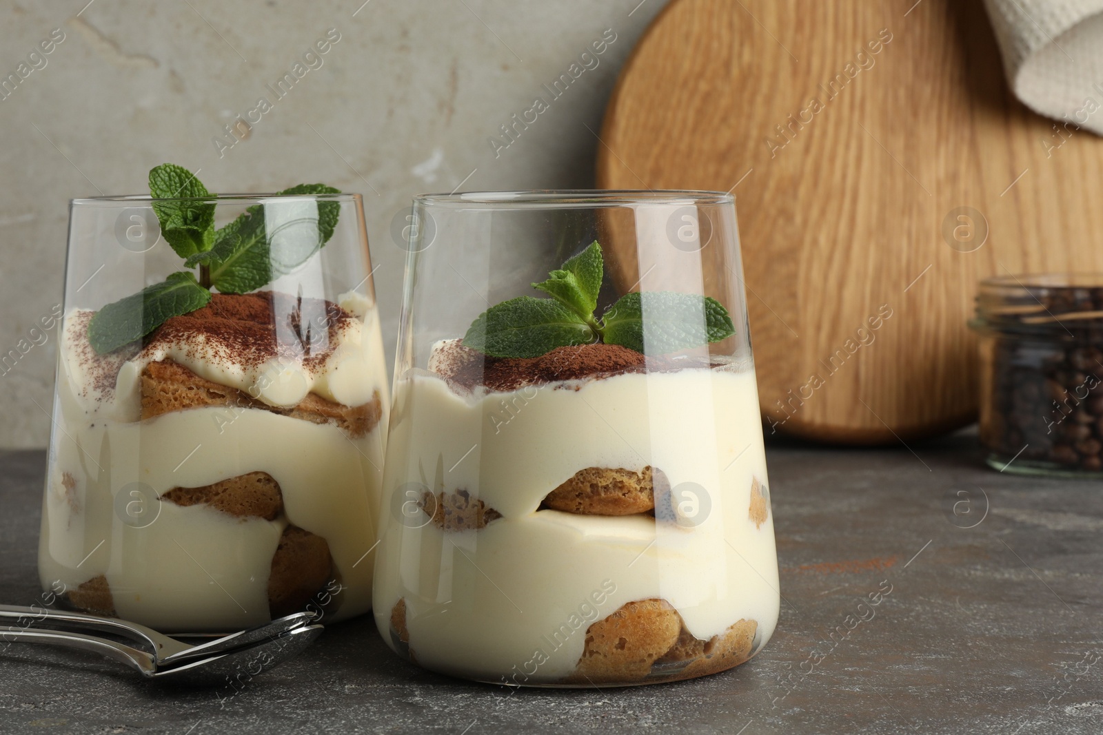 Photo of Delicious tiramisu with mint in glasses on grey table