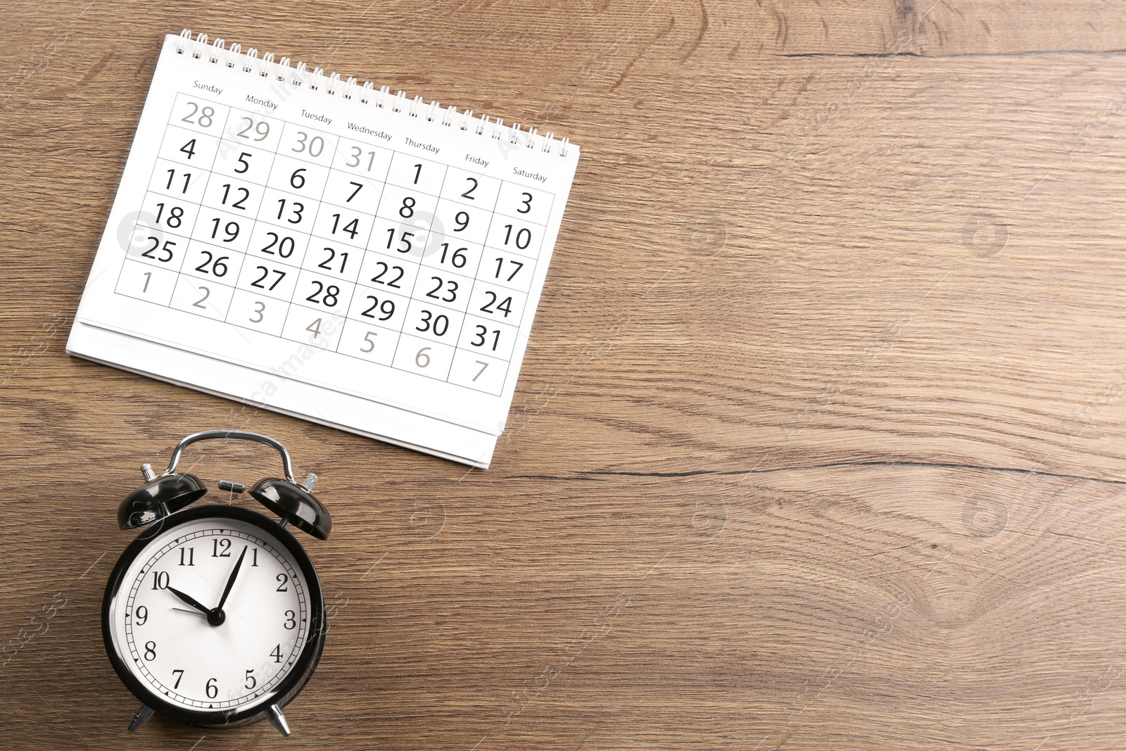 Photo of Calendar and alarm clock on wooden table, flat lay. Space for text