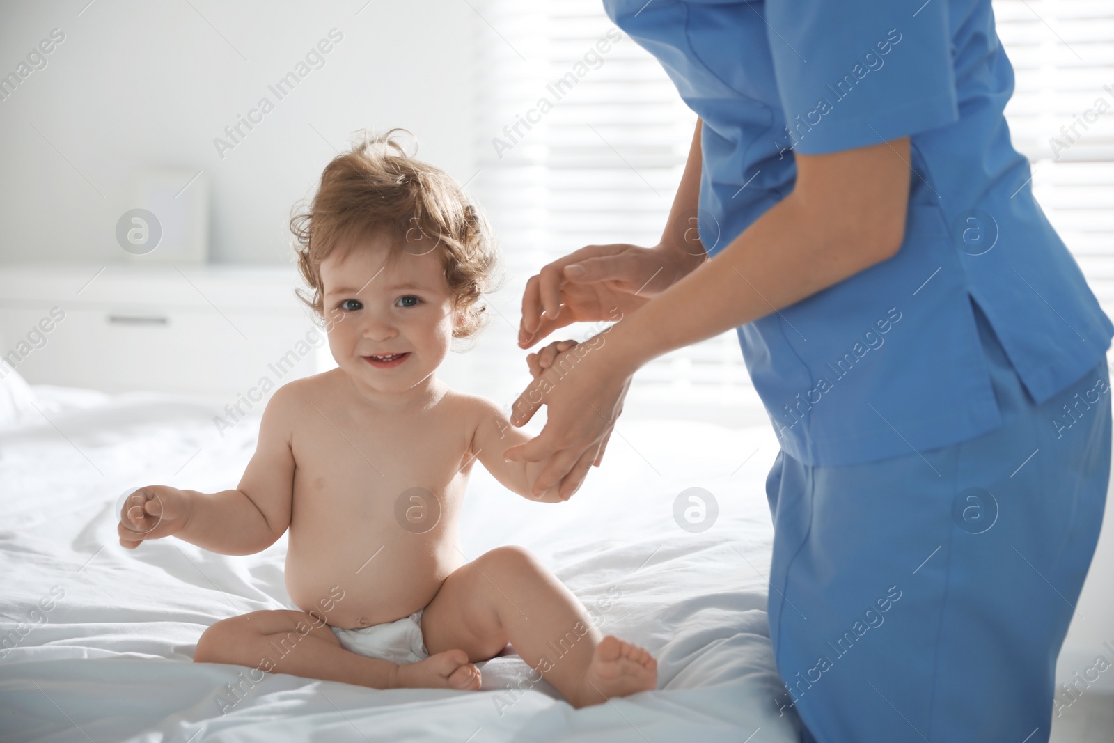 Photo of Orthopedist examining little baby on bed indoors