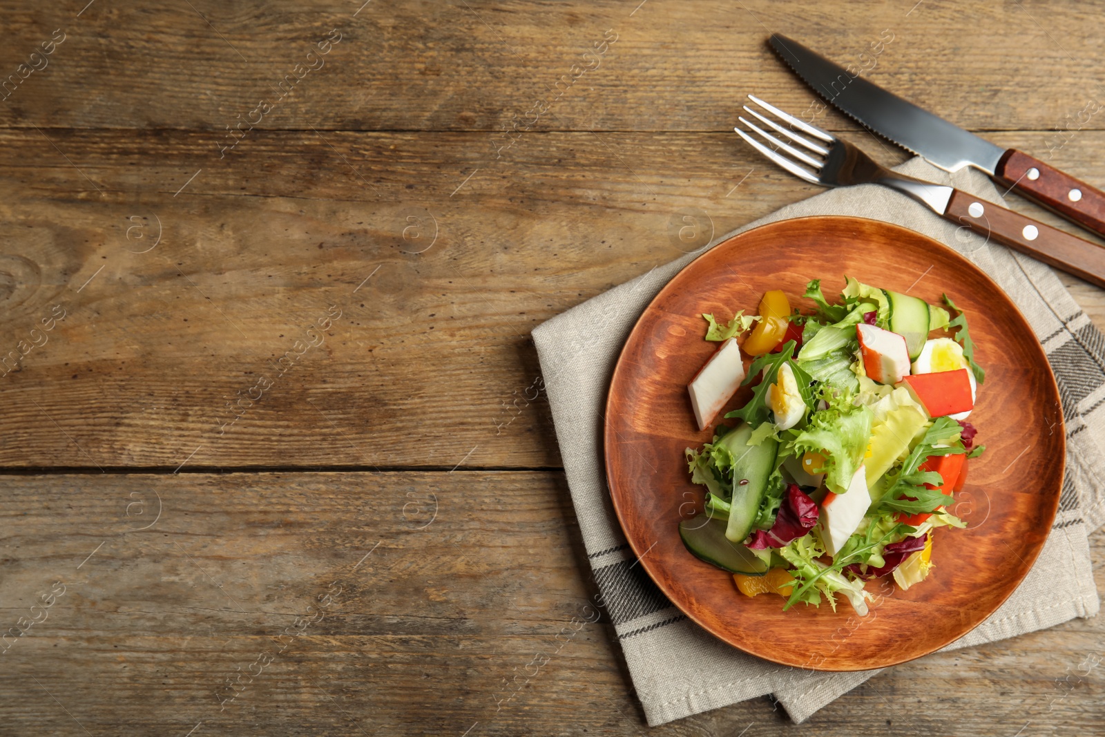 Photo of Delicious salad with crab sticks and lettuce served on wooden table, flat lay. Space for text