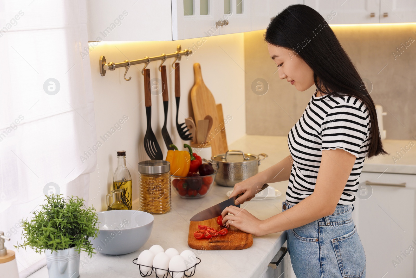 Photo of Cooking process. Beautiful woman cutting tomato in kitchen