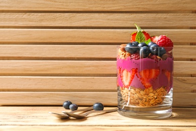 Delicious acai dessert with granola and berries in glass on wooden table. Space for text