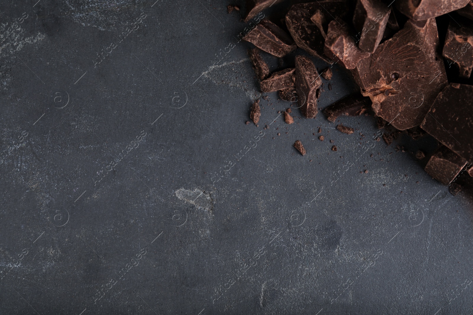 Photo of Pieces of tasty dark chocolate on grey table, top view. Space for text