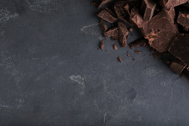 Pieces of tasty dark chocolate on grey table, top view. Space for text