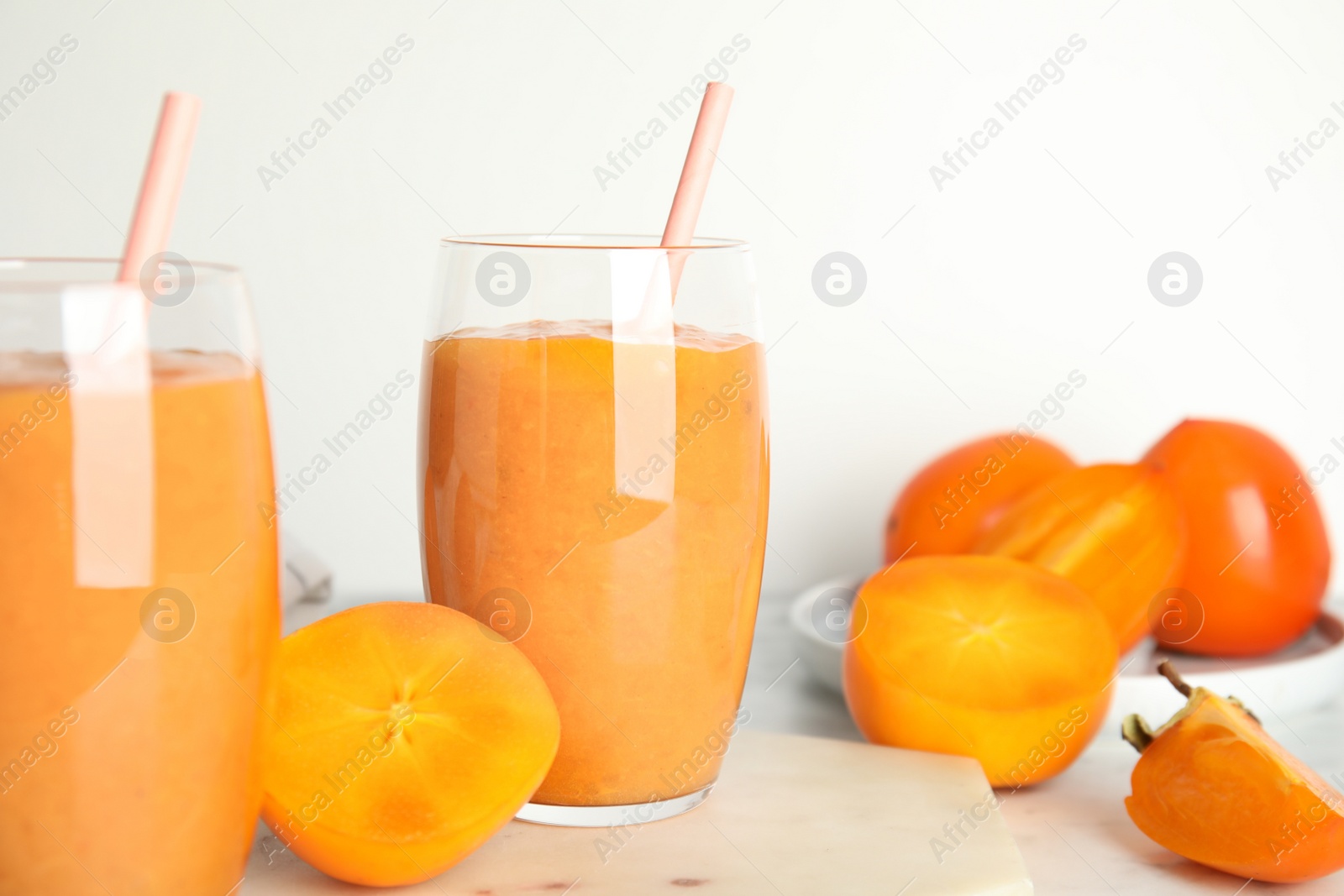 Photo of Tasty persimmon smoothie with straw on marble board against white background