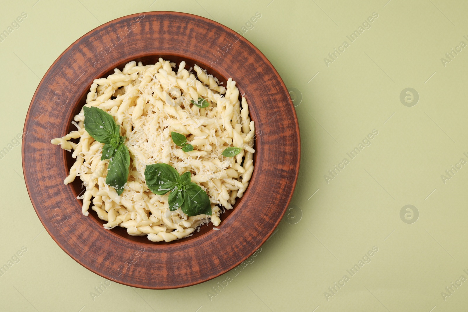 Photo of Plate of delicious trofie pasta with cheese and basil leaves on light olive background, top view. Space for text