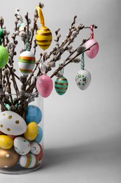 Photo of Vase with beautiful willow branches and painted Easter eggs on light grey background, closeup