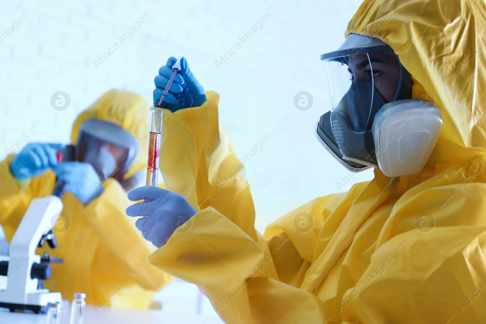 Photo of Scientist in chemical protective suit dripping blood  into test tube at laboratory. Virus research