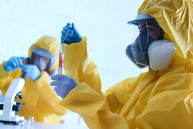 Photo of Scientist in chemical protective suit dripping blood  into test tube at laboratory. Virus research