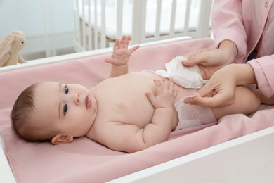 Mother changing baby's diaper on table at home