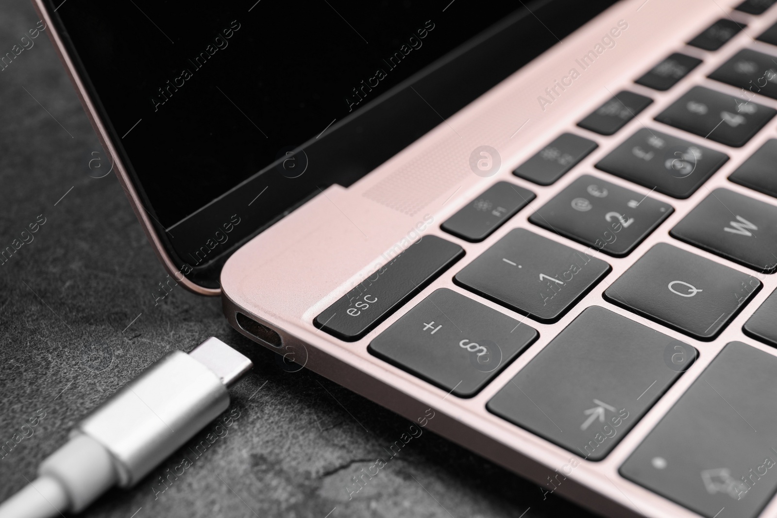 Photo of USB cable with type C connector and laptop on grey table, closeup