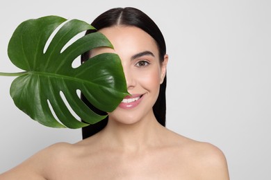 Photo of Woman holding leaf of monstera on light grey background. Spa treatment