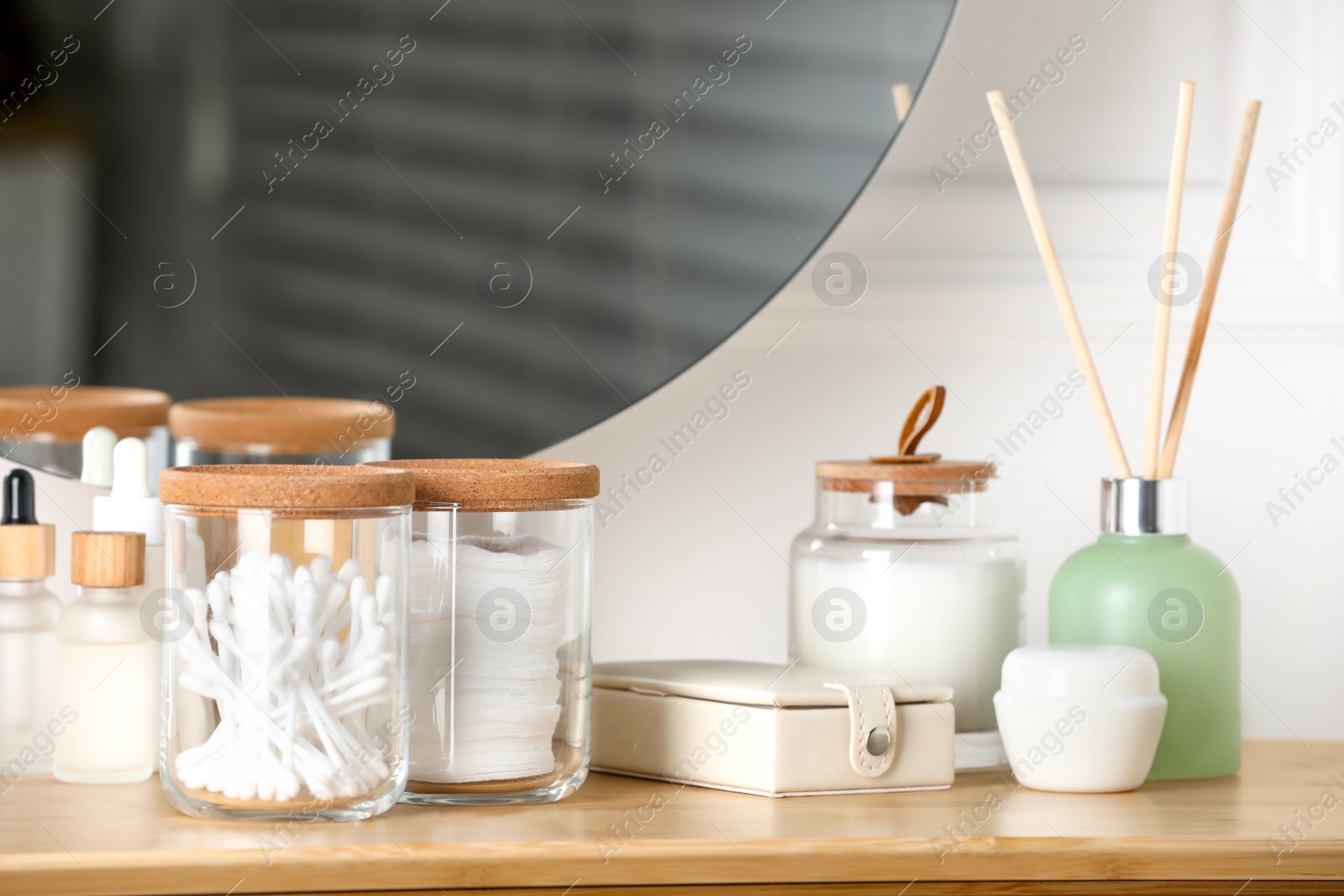 Photo of Glass jars with cotton swabs and pads near cosmetic products on dressing table