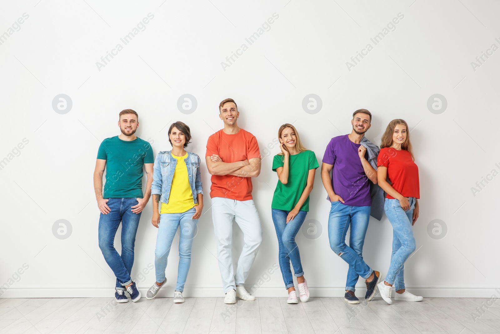Photo of Group of young people in jeans and colorful t-shirts near light wall