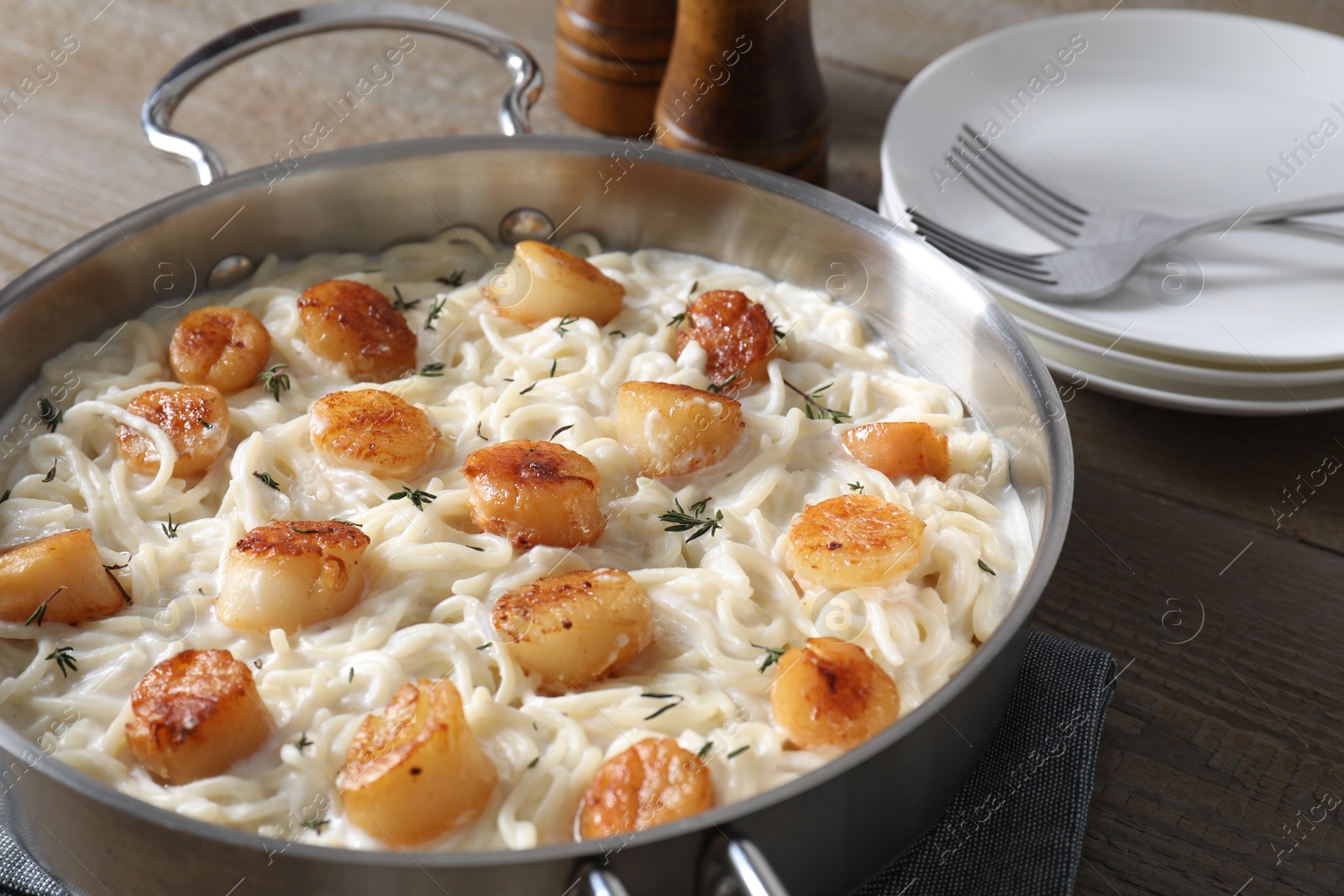 Photo of Delicious scallop pasta served on wooden table, closeup