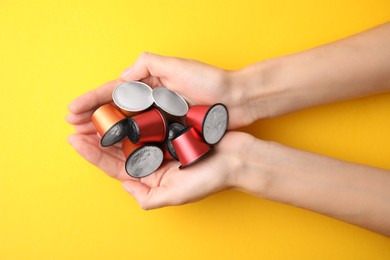 Woman holding heap of coffee capsules on yellow background, top view