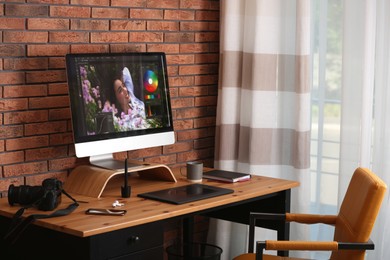 Photo of Modern retoucher's workplace with different digital devices on wooden table near red brick wall