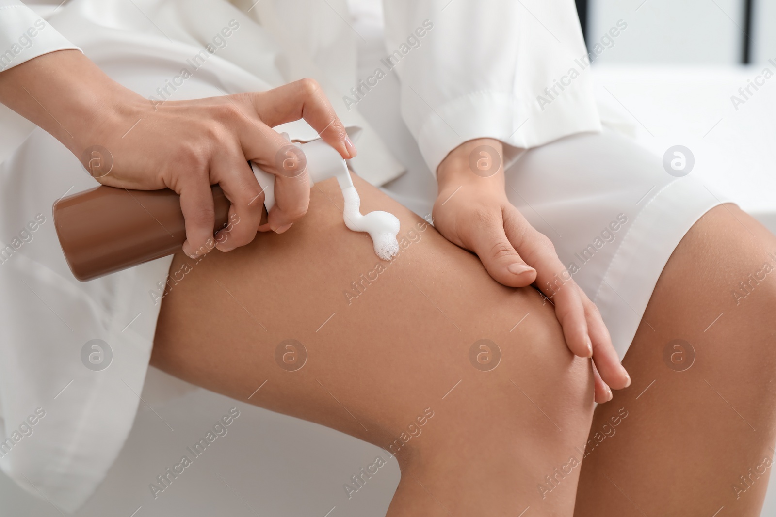 Photo of Woman applying self-tanning product onto leg indoors, closeup