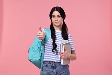 Photo of Student with books and backpack showing thumb up on pink background
