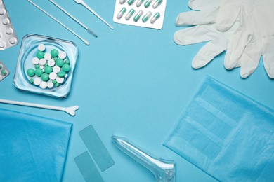 Photo of Frame of disposable gynecological examination kit and pills on light blue background, flat lay. Space for text