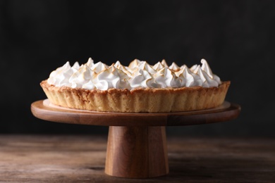 Stand with delicious lemon meringue pie on wooden table against black background