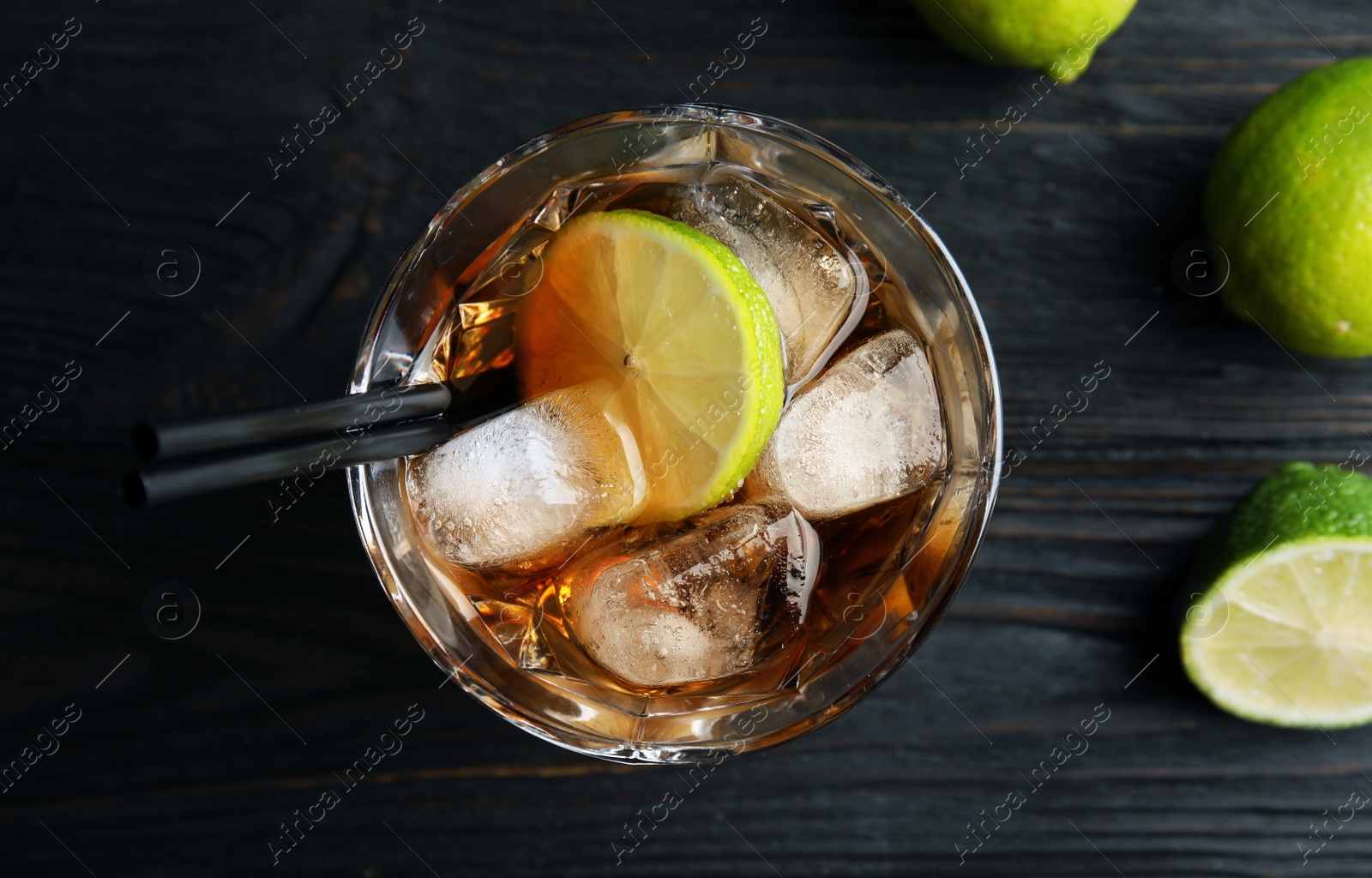 Photo of Glass of cocktail with cola, ice and cut lime on wooden background, top view