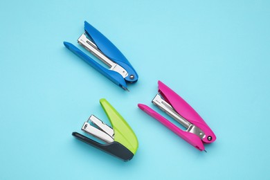 Photo of New bright staplers on light blue background, flat lay. School stationery