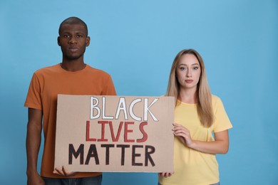 Young woman and African American man holding sign with phrase Black Lives Matter on light blue background. Racism concept