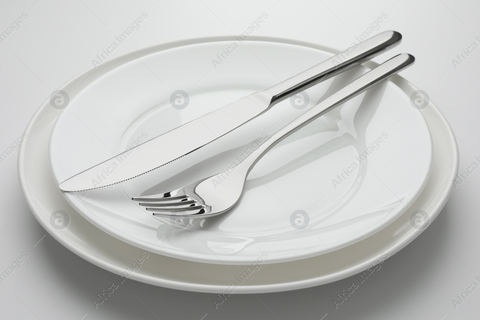 Photo of Clean plates, fork and knife on white background, closeup