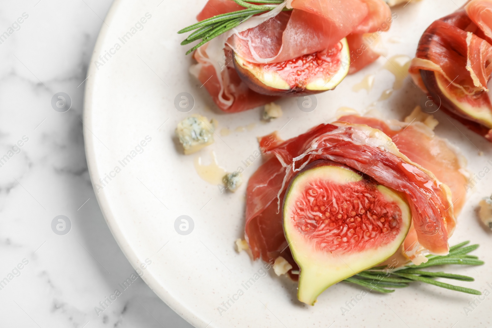 Photo of Delicious ripe figs and prosciutto served on white marble table, closeup