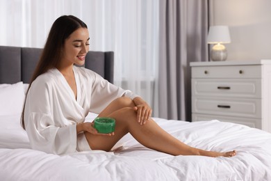Photo of Young woman applying aloe gel onto her leg on bed indoors