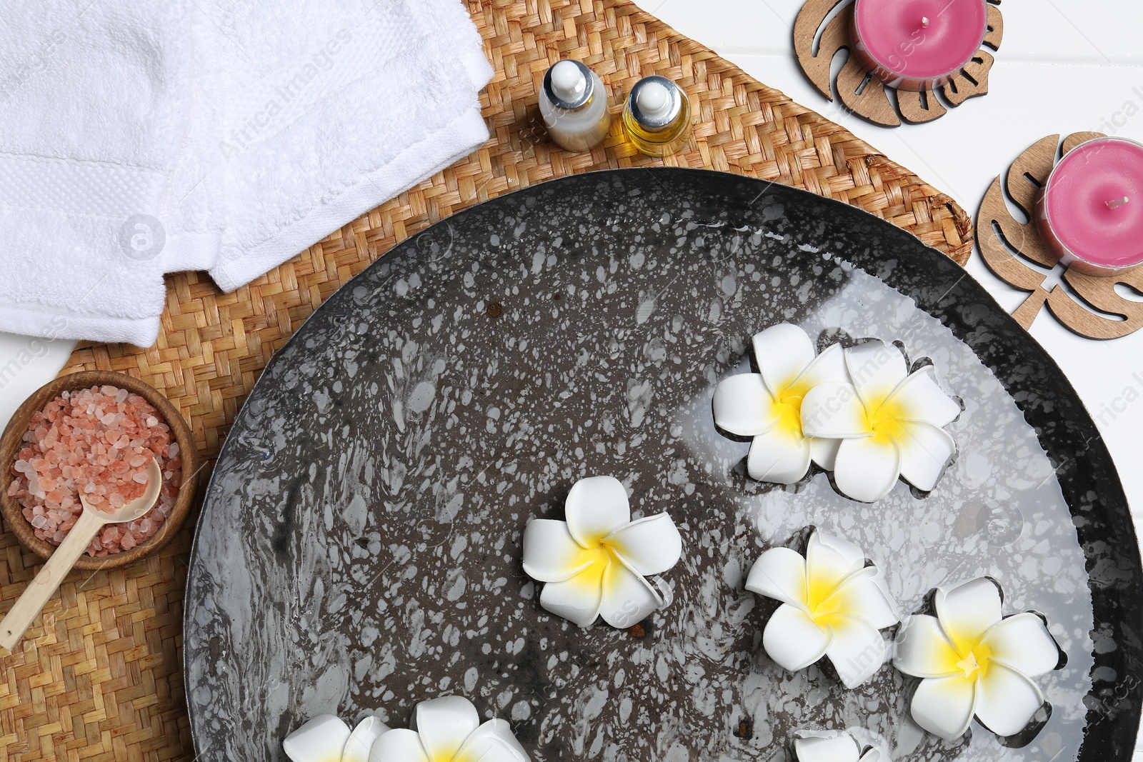 Photo of Bowl of water with plumeria flowers and different spa supplies on table, top view